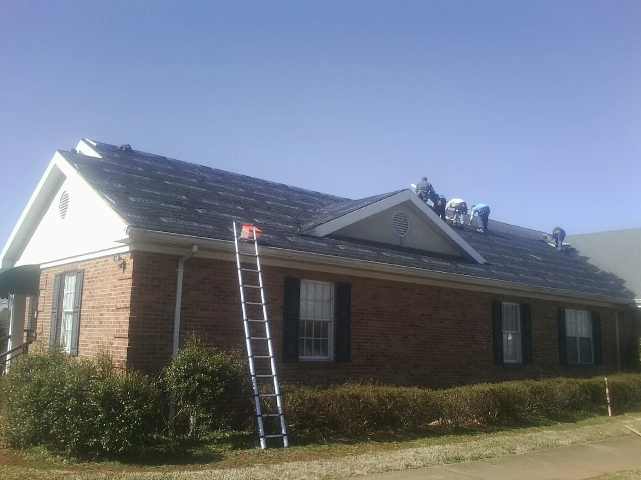 Crew tearing shingles off a brick ranch roof with a ladder set — Emergency Roof Repair work by our crew in Lewisburg
