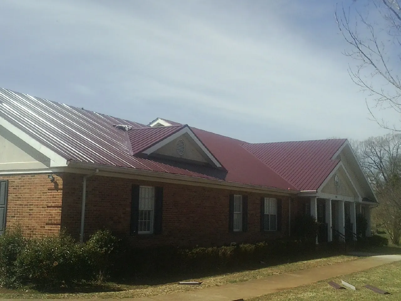 Red metal roof with gabled entries on a long brick building, from a Hail Damage Roof Repair job in Lewisburg